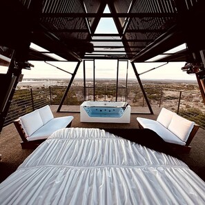 A modern room with a large bed, two white sofas, a hot tub, and a view of a desert landscape. - Stunning A-Frame with Folding Glass Walls & Open-Air Living in Cottonwood, Texas (Cottonwood Shores)