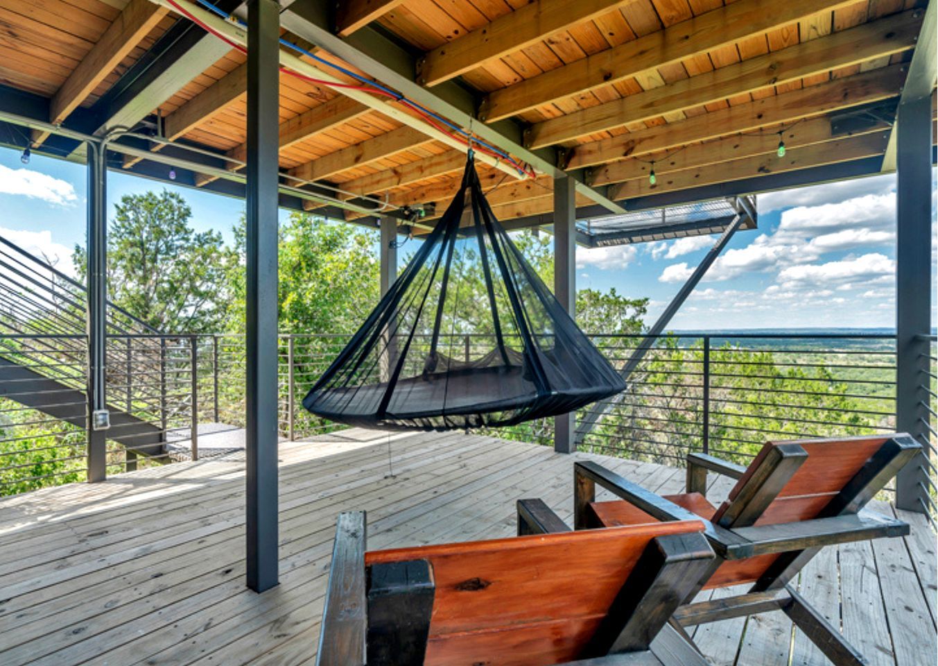 Une terrasse en bois avec un fauteuil suspendu et une vue sur le paysage.