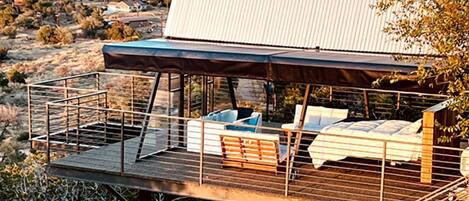 Une terrasse extérieure moderne, dotée d’un espace salon et d’une zone couverte, offrant une vue sur un paysage désertique.