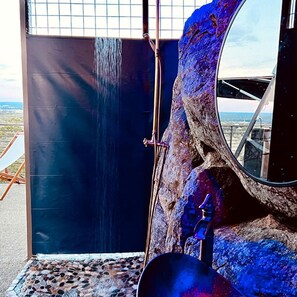 A bathroom with a large mirror, a shower, and a view of the landscape.
