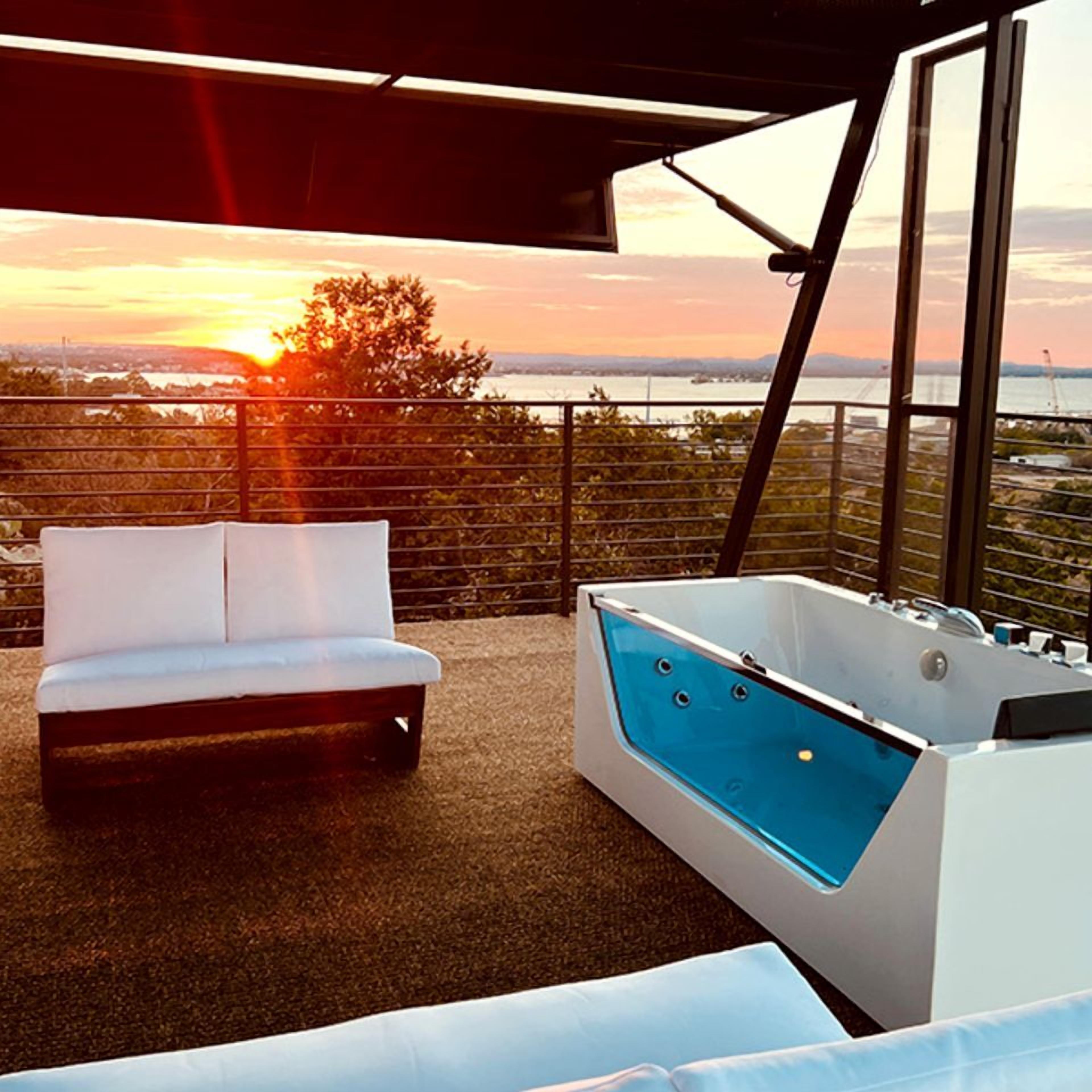 Un balcón con sofá blanco y un jacuzzi, con vistas a la puesta de sol.