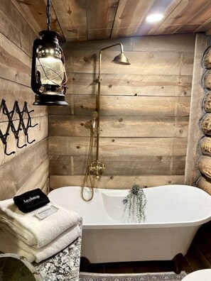 Ein Badezimmer in einer Holzhütte mit freistehender Badewanne, einer hängenden Laterne und einem Handtuchhalter.