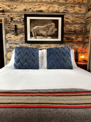 A bed with a white mattress, two blue patterned pillows, a framed picture of a horse, and a stone wall. - Serene Western Cabin with 23 Private Acres & Stargazing Near Zion National Park, Mount Carmel, Utah (Mount Carmel)
