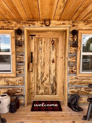 Entrada a una cabaña de madera rústica, con puerta, ventanas y felpudo.