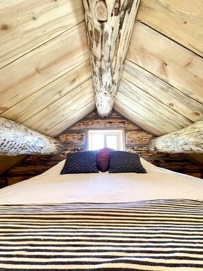 Een kamer met een schuine plafond, een bed met gestreept beddengoed en een raam met uitzicht.
