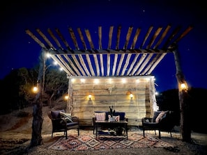 An outdoor seating area with a pergola, rustic wooden walls, and wall-mounted lights. - Serene Western Cabin with 23 Private Acres & Stargazing Near Zion National Park, Mount Carmel, Utah (Mount Carmel)