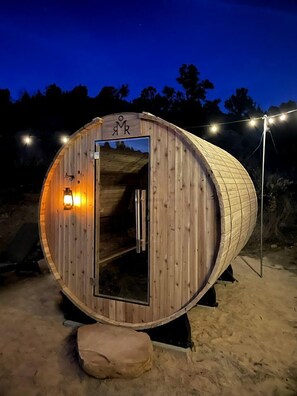 Eine holzverkleidete, fassförmige Struktur mit Tür, einer kleinen Lampe und einem Metallrahmen.
