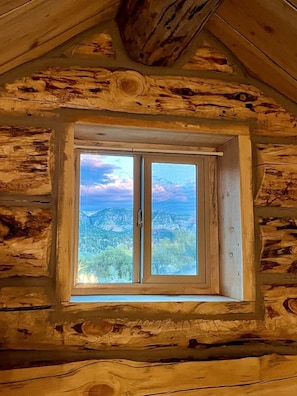 Het interieur van een blokhut met een raam dat uitzicht biedt op een bergachtig landschap.