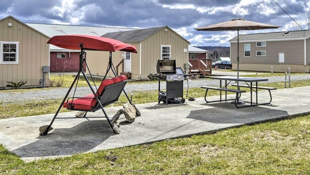 Een terras met een hangstoel, picknicktafel, barbecue en parasol.