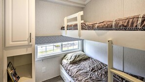 Een stapelbed met een raam, een witte kast en een klein plankje met boeken.