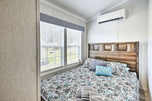 Ein Schlafzimmer mit einem Bett, einem Fenster mit Jalousien, einer Klimaanlage und einem hölzernen Kopfteil.