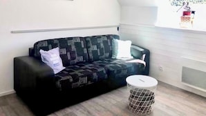Un salon moderne avec un canapé noir à motifs, une petite table ronde, un tableau accroché au mur et une fenêtre donnant sur un paysage enneigé.