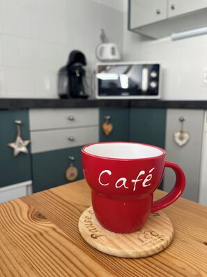 Une tasse rouge sur laquelle est inscrit le mot « Café », posée sur un sous-verre en bois avec du texte.