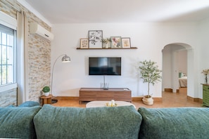 A living room with a TV, sofa, and decorative items. - Villa Manantial Country House in the Seville Countryside (La Puebla de Cazalla)