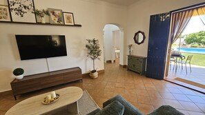 A living room with a flat-screen TV, a sofa, a coffee table, a potted plant, a cabinet, and a view of a swimming pool through a glass door. - Villa Manantial Country House in the Seville Countryside (La Puebla de Cazalla)
