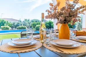 A table set for dining with plates, cutlery, and a bottle of white wine, with a vase of dried flowers and a view of a pool and greenery. - Villa Manantial Country House in the Seville Countryside (La Puebla de Cazalla)