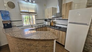 A kitchen with granite countertops, a built-in brick island, a stainless steel range hood, a white refrigerator, and wooden cabinets. - Villa Manantial Country House in the Seville Countryside (La Puebla de Cazalla)