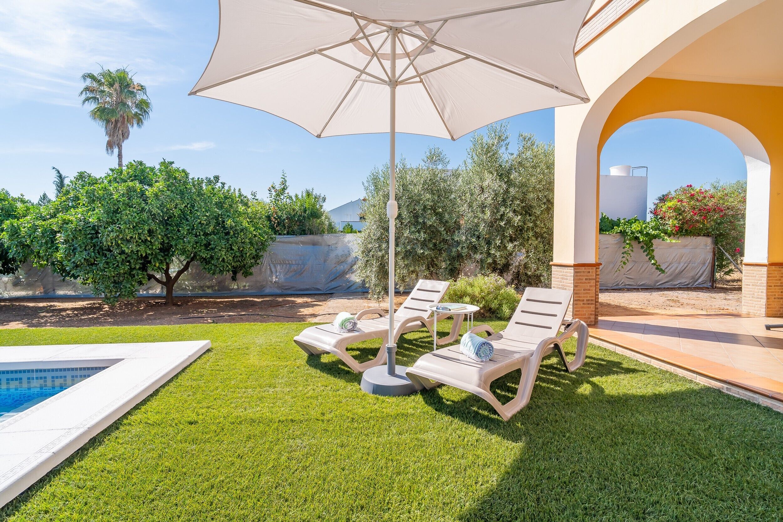 A poolside area with lounge chairs, a large umbrella, and a clear view of the sky.