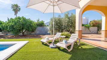 A poolside area with lounge chairs, a large umbrella, and a clear view of the sky.