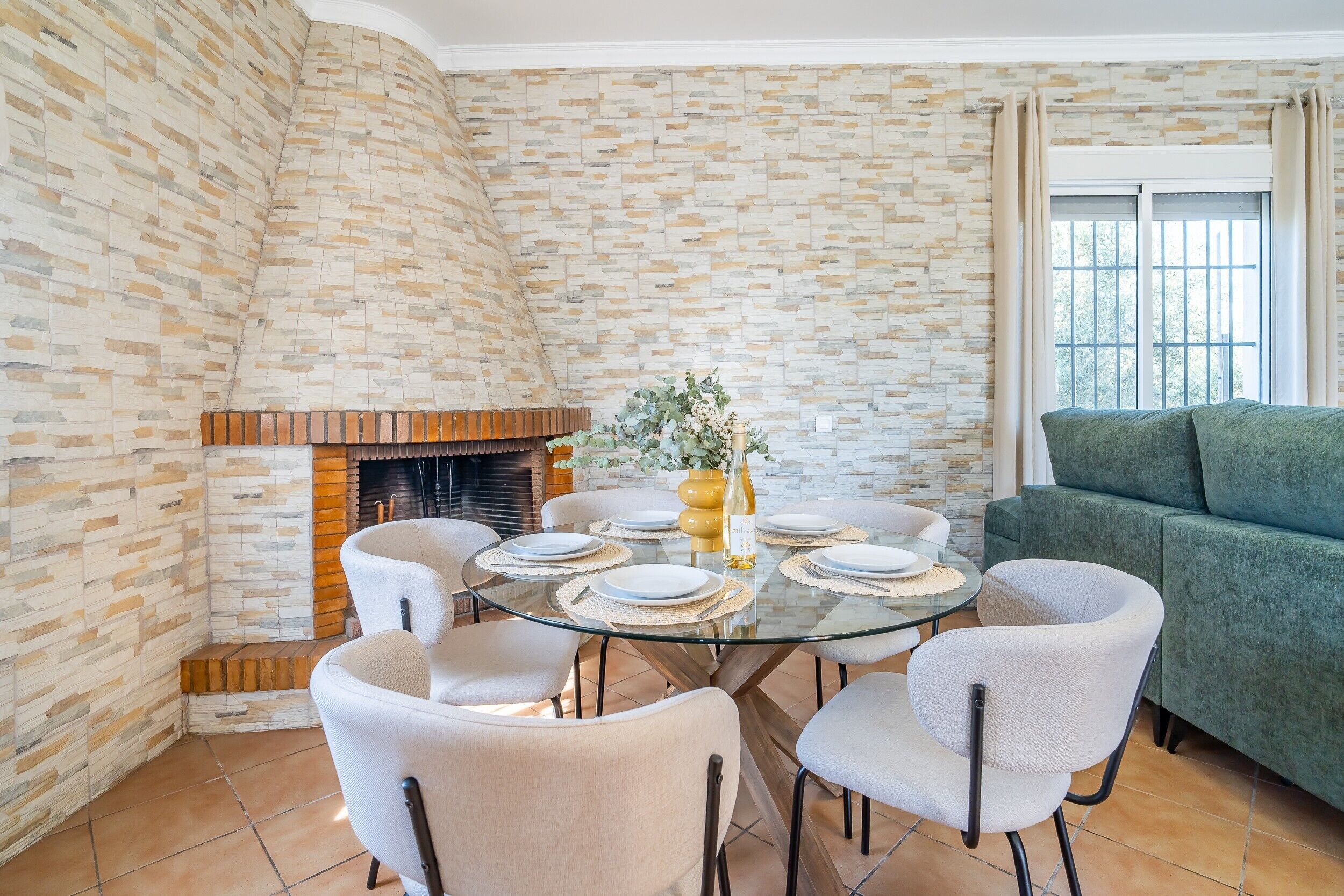Un comedor con una mesa de vidrio, sillas blancas, una chimenea de ladrillo y un sofá verde.