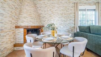 Un comedor con una mesa de vidrio, sillas blancas, una chimenea de ladrillo y un sofá verde.