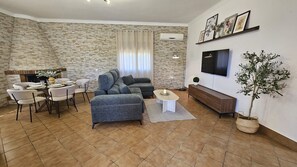 A living room with a stone wall, a sofa, a TV, a dining table with chairs, and a potted plant. - Villa Manantial Country House in the Seville Countryside (La Puebla de Cazalla)