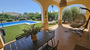 Un patio con una mesa, sillas, una hamaca colgante y vistas a una piscina.