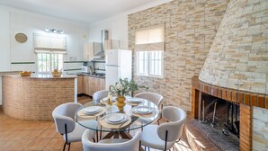Una cocina moderna con una isla de ladrillo, un área de comedor con mesa de vidrio y una chimenea con pared de piedra.