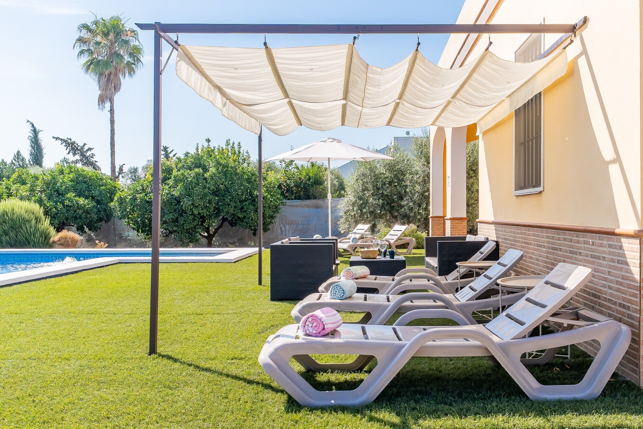 Un espace aménagé au bord de la piscine, avec des chaises longues, une pergola et une piscine.