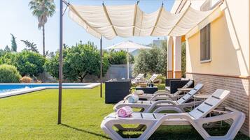 Un espace aménagé au bord de la piscine, avec des chaises longues, une pergola et une piscine.