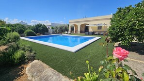 Una piscina rectangular rodeada de césped artificial verde, con un edificio con ventanas de arco en el fondo.