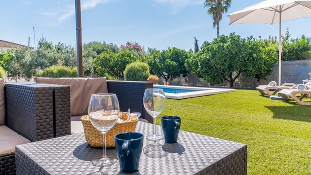 Un área de estar al aire libre con mobiliario de mimbre, una piscina y un césped.