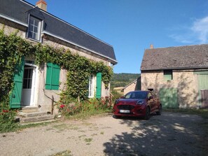 Una casa amb persianes verdes, un cotxe vermell estacionat al davant i un camí d'accés de grava.