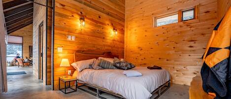 A cozy cabin-style bedroom with a bed, bedside lamps, and a cowhide rug.