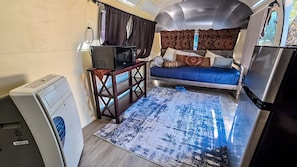 A compact living space with a bed, a microwave, a small table, and a refrigerator.