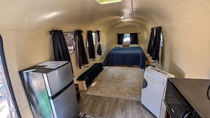 A compact RV interior with a kitchenette, a bed, and a small seating area.