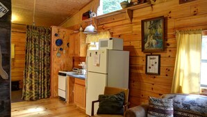 Interior de cabaña con paredes de madera, una kitchenette, comedor y ventana con cortinas.