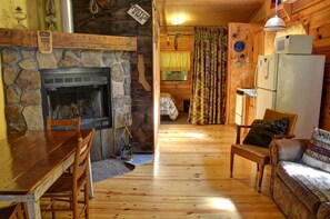 A cozy cabin interior with a stone fireplace, wooden furniture, a dining table, a sofa, and a refrigerator. - Cozy Log Cabin for Getaway in the Mountains near Cherokee, North Carolina (Cherokee)