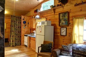 A cabin interior with wooden walls, a kitchenette, a dining area, and a window with curtains. - Cozy Log Cabin for Getaway in the Mountains near Cherokee, North Carolina (Cherokee)