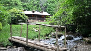 Un puente de madera sobre un arroyo que lleva a una cabaña con porche y chimeneas.
