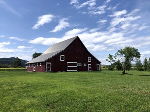 Ein rotes Bauernhaus mit weißer Garagentür, umgeben von einer Wiese und einigen Bäumen.