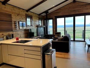 A modern kitchen with a large island, a dining area with a couch, and a view of the countryside through large windows. - Luxury Flathead Lake Cabin with Stunning Views (Somers)