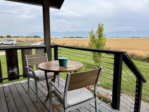 A wooden deck with a table and chairs, overlooking a field and mountains. - Luxury Flathead Lake Cabin with Stunning Views (Somers)