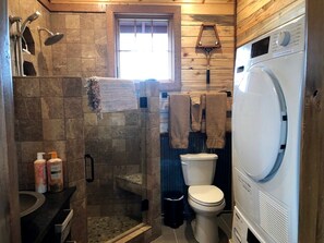 Ein Badezimmer mit einer Duschkabine aus Stein, einer Toilette, einer Waschmaschine und einem Fenster.