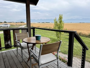 A wooden deck with a table and chairs, overlooking a field and mountains. - Luxury Flathead Lake Cabin with Stunning Views (Somers)