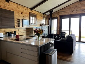 A modern kitchen with wooden walls, a central island, and a dining area with a sofa and table. - Luxury Flathead Lake Cabin with Stunning Views (Somers)