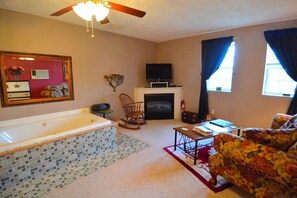 A living room with a fireplace, a television, a rocking chair, a sofa, and a large mirror. - Romantic Suite Rental with a Hot Tub near Savage River State Forest, Maryland (Oakland)