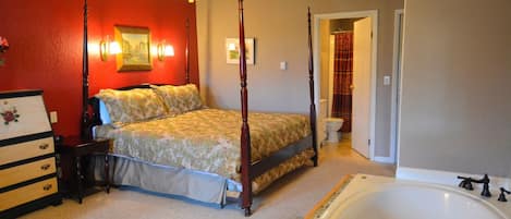 Una cama con dosel, un edredón floral, un aparador de madera con cajones, una bañera grande y un ventilador de techo.