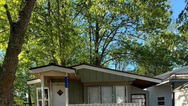 A single-story house with a porch, a large wheel, and a barrel. - Cozy Riverfront RV Retreat with Seasonal Pool & Trout Fishing near Hiawassee, Georgia (Hiawassee)