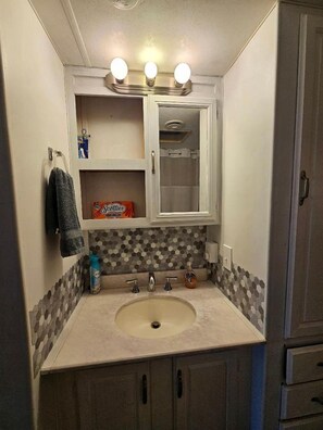 Une salle de bain avec un lavabo, un miroir et trois lampes au-dessus du miroir.